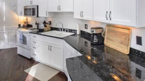 A modern kitchen with white cabinetry, a black granite countertop, and a built-in microwave. - Charming 2BR in Historic Savannah! (Savannah)