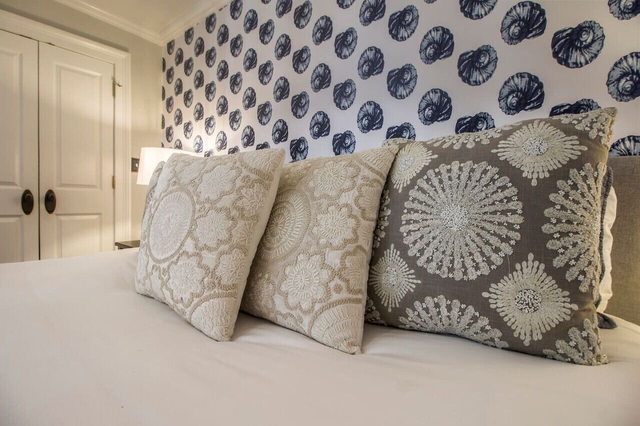 Una cama con tres almohadas, una puerta blanca y un papel tapiz estampado.