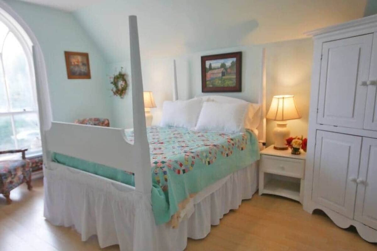 A bedroom with a four-poster bed, a nightstand with a lamp, and a wardrobe.