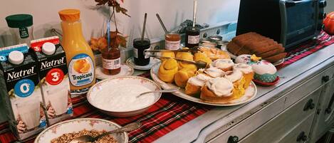 Una mesa de desayuno con diversos alimentos, como un tazón de cereales, un plato de pasteles y varios condimentos.