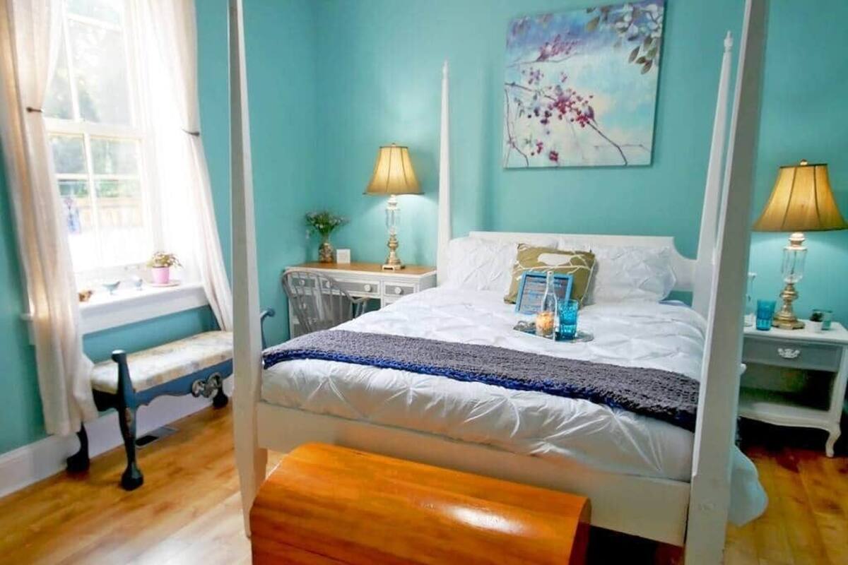 A four-poster bed with a white canopy, a bench at the foot of the bed, and a nightstand with a lamp.