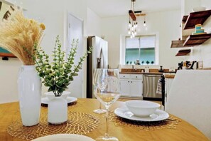 Un coin repas avec une table en bois, des assiettes blanches, un verre de vin blanc et un vase contenant des plantes vertes.