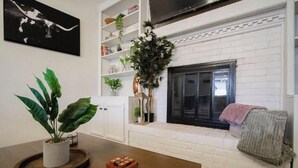 A living room with a fireplace, white brick walls, and a wooden coffee table with a plant and a game. - Single-Story Charmer! 5BR! Pet Friendly Getaway

 (Indianapolis)