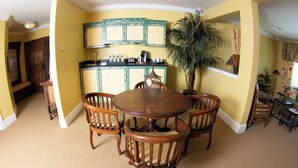A dining area with a round wooden table and four chairs, a kitchen with a green cabinet, and a large potted plant. - Keyah Grande - South Pacific (Pagosa Springs)