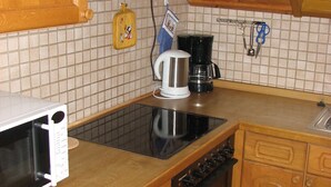 A kitchen with a microwave, stove, coffee maker, and a clock on the wall. - Haus Jägerwinkel - Wohnung II (Müllheim im Markgräflerland)