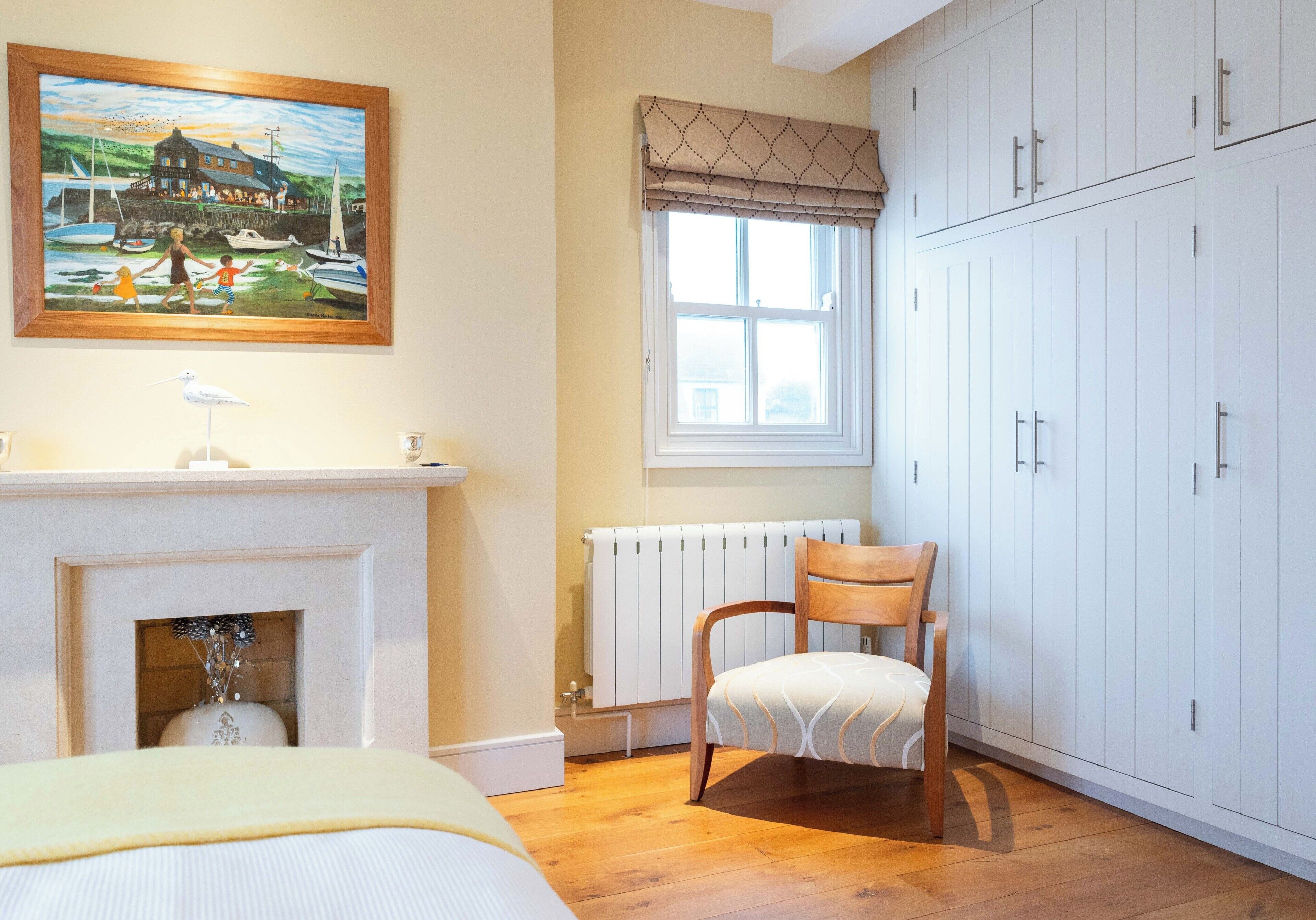 Ein Schlafzimmer mit Bett, Gemälde, Fenster mit Vorhängen, Heizkörper und Kleiderschrank.