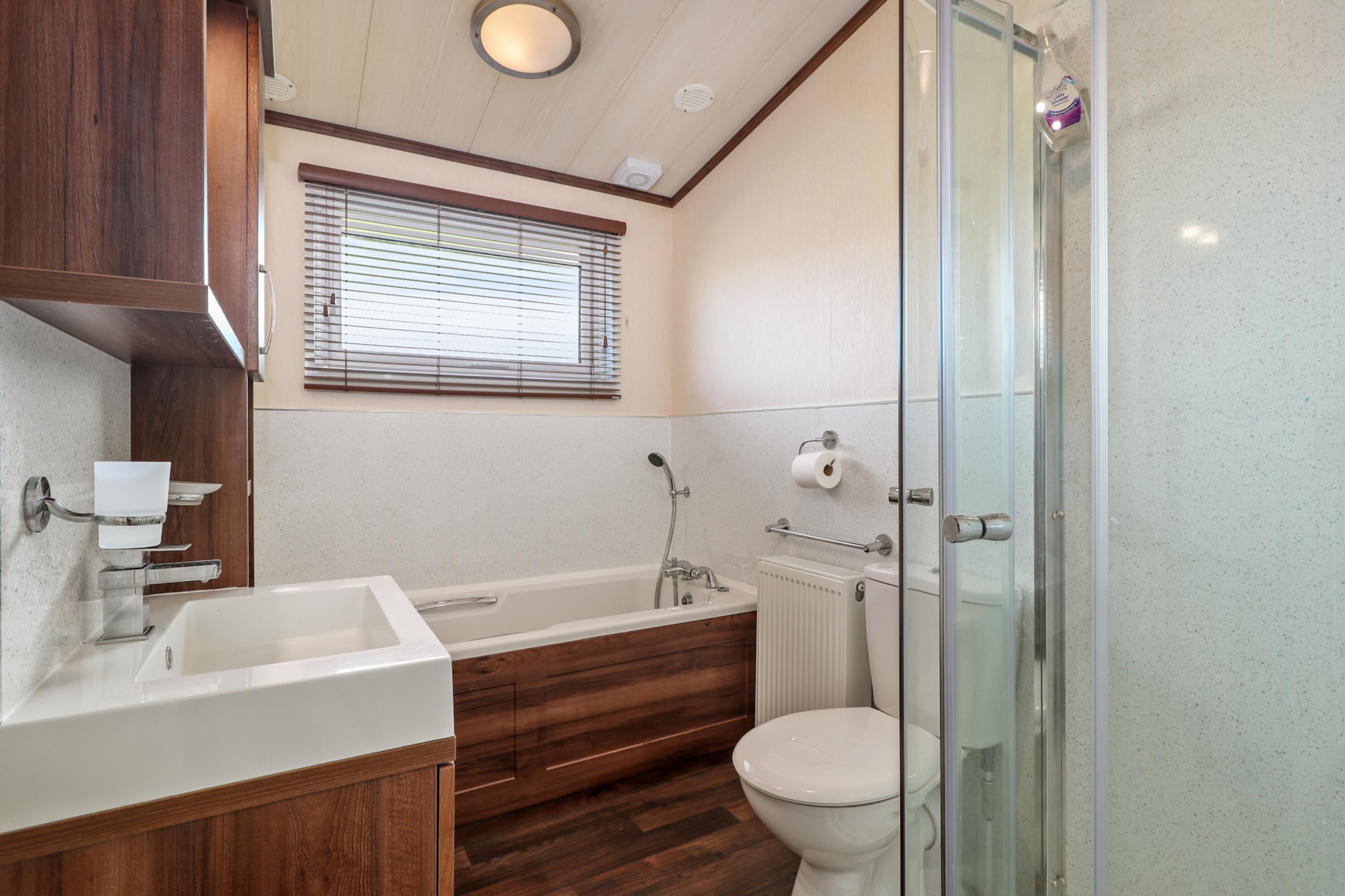 Un baño moderno con tocador de madera, bañera independiente, inodoro y cabina de ducha de vidrio.