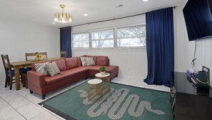 A living room with a sectional sofa, a dining table, and a TV. - Brand new*Walk to Graceland*Sleeps 10* (Memphis)