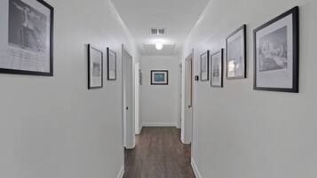 Un couloir avec des tableaux encadrés accrochés aux murs, un plancher en bois et un luminaire au plafond.