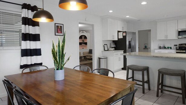 Une cuisine moderne avec des meubles blancs, une table à manger en bois et des luminaires suspendus.
