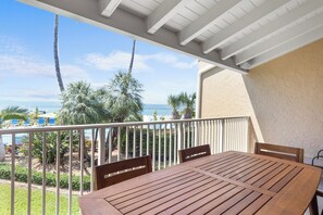 A wooden table and chairs on a balcony with a view of the ocean and palm trees. - Relaxed and Easy Oceanfront Townhouse (Key Colony Beach)