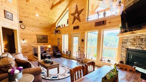 A cozy log cabin interior with a fireplace, wooden furniture, and large windows offering mountain views. - A Tyme to Chill (Sevierville)