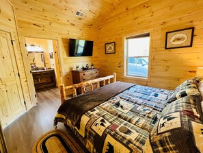 A wooden cabin bedroom with a large bed, a dresser, a television, and a window. - A Tyme to Chill (Sevierville)