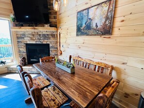 A wooden dining area with a fireplace, a television mounted on the wall, and a painting of a forest scene. - A Tyme to Chill (Sevierville)