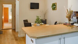 Una cocina moderna con encimera de madera, armarios blancos, un televisor de pantalla plana montado en la pared y una pequeña planta en maceta sobre la encimera.
