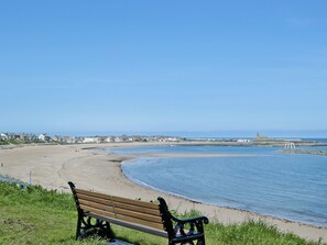A bench overlooking a beach with a clear view of the sea and a distant church. - Escape to The Carriage House in picturesque Newbiggin by the Sea. (Newbiggin by the Sea)