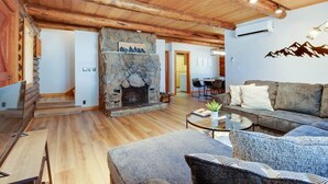 A spacious living room with a stone fireplace, wooden ceiling beams, and a cozy seating area with a sofa and armchairs.