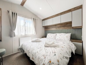 Un dormitorio con cama, radiador, ventana con cortinas y cabecera de madera.