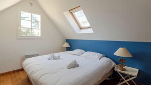 Een slaapkamer met een schuine kap, een dakraam, een bed met witte lakens, twee nachtkastjes met lampen en een raam.