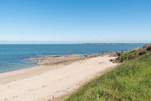 A sandy beach with clear blue water and a grassy area.