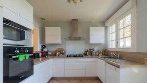 Een moderne keuken met witte kasten, een Bosch oven, een gasfornuis en een raam met zonwering.