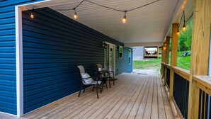 A covered porch with a wooden deck, a table with chairs, and string lights. - Red River Gorge, Hollerwood Stays! High Speed Wi-Fi, Pet-Friendly! New Home! (Clay City)