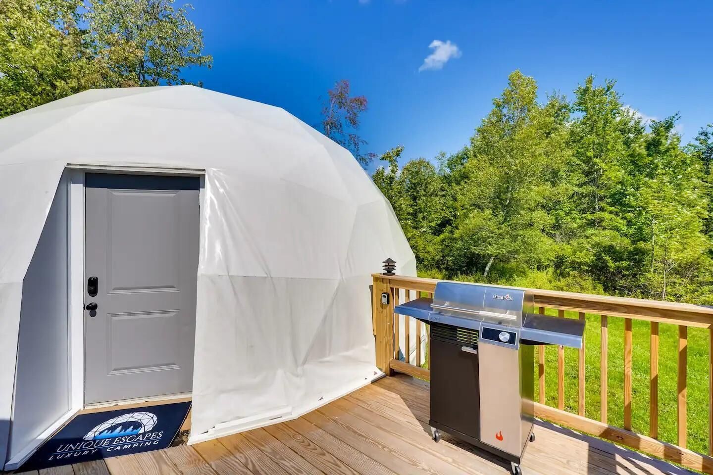 A dome-shaped tent with a door, a barbecue grill on a deck, and a sign indicating luxury camping.