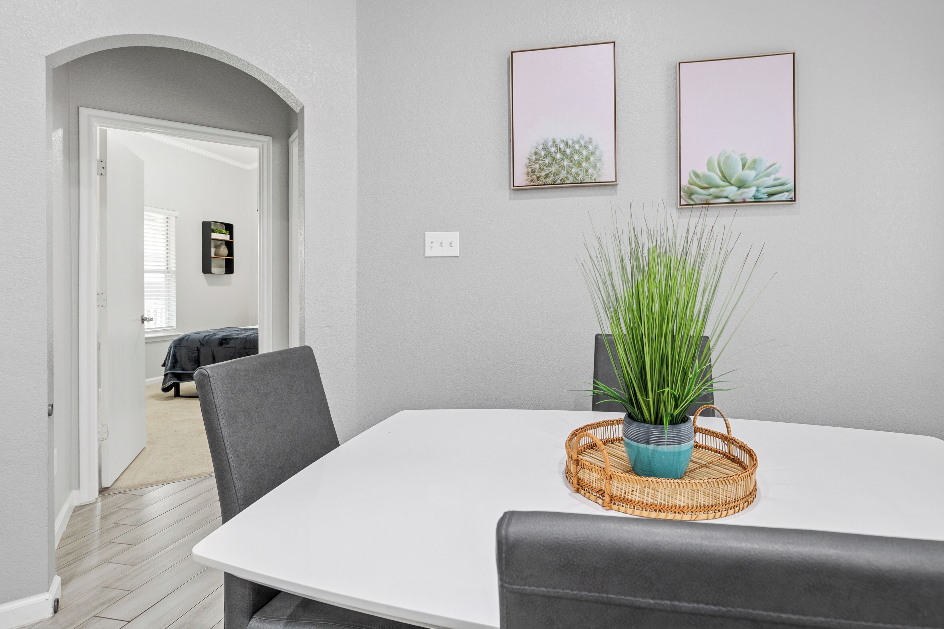 Un coin repas avec une table blanche, des chaises grises, un panier en osier contenant une plante et deux tableaux encadrés accrochés au mur.