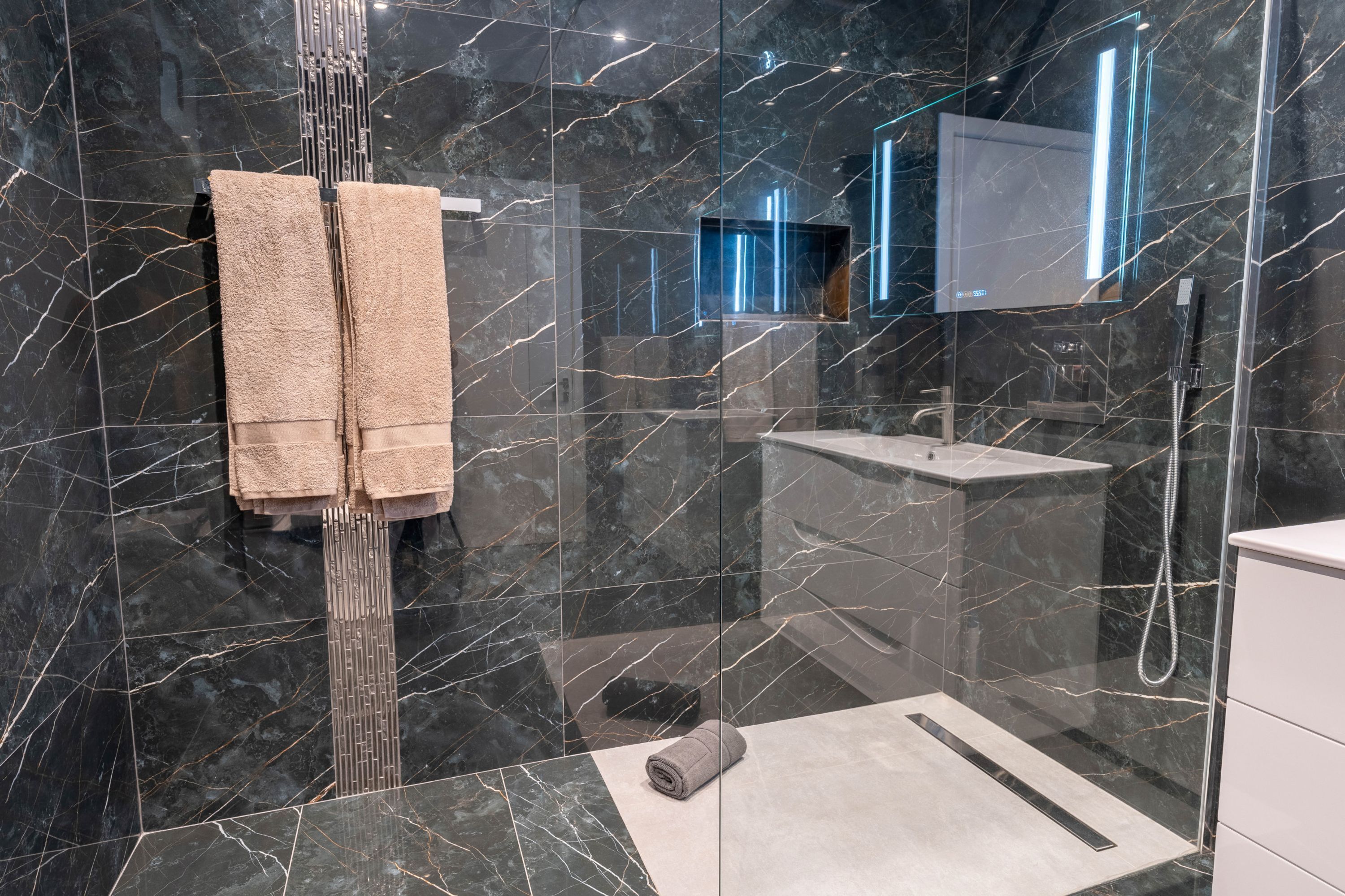 A modern bathroom with a glass shower enclosure, marble walls, and a large mirror.