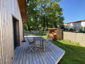 A wooden deck with a table and chairs, a wooden playhouse, and a fenced yard. - 143 - charming new timber-framed house for 8 people (HOURTIN)