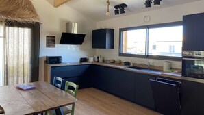 Een moderne keuken met donkere kastjes, een houten eettafel en een groot raam dat natuurlijk licht binnenlaat.