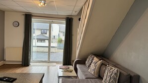 A modern living room with a sofa, a coffee table, and a view of the street through a glass door.
