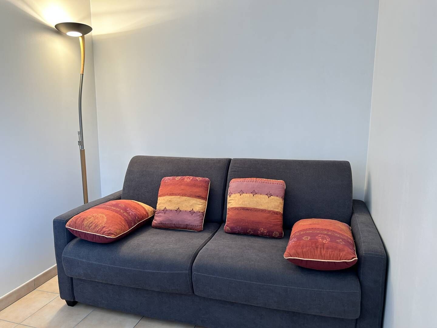 Um sofá azul escuro com quatro almofadas decorativas em um quarto com um abajur.