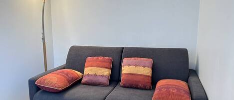 Um sofá azul escuro com quatro almofadas decorativas em um quarto com um abajur.