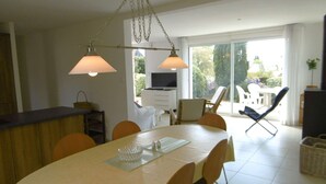 A dining area with a table set for four, a television in the background, and a view of the outdoors through large windows.