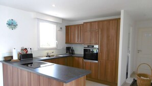 A modern kitchen with wooden cabinets, a central island, a built-in oven, and a window providing natural light.