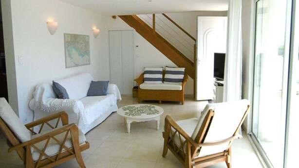 A spacious living room with a white sofa, two wooden chairs, a small coffee table, and a wooden staircase leading to another room.