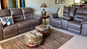 Un salon avec deux canapés en cuir marron, un pouf à motifs, une lampe et un tapis.