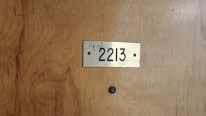 Een houten deur met een metalen plaatje waarop het nummer 2213 staat.