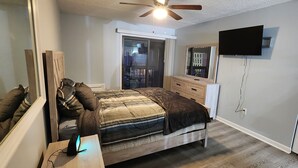 Een slaapkamer met een bed, een dressoir, een aan de muur bevestigde televisie en een plafondventilator.
