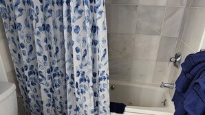 Een badkamer met toilet, bad en douchegordijn met een bladmotief.
