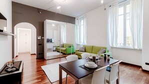 A modern living room with a dining area, a green sofa, and a kitchen in the background. - All in One - MyHomeinComo (Como)