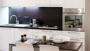 A modern kitchen with a gas stove, stainless steel oven, and a dining area with white chairs and a table set for two. - All in One - MyHomeinComo (Como)
