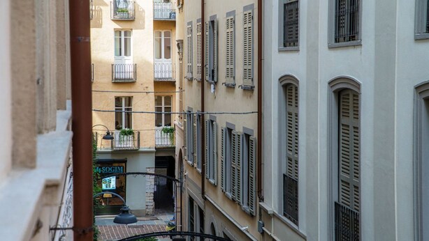 A narrow alleyway with buildings on either side, a visible storefront with a sign, and a street lamp. - All in One - MyHomeinComo (Como)