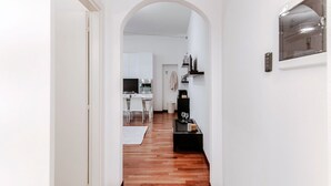 A hallway leading to a kitchen with white cabinets, a dining table, and a black coffee machine. - All in One - MyHomeinComo (Como)