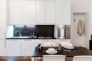 Una cocina moderna con armarios blancos, encimera oscura y un área de comedor con una mesa dispuesta para dos personas.