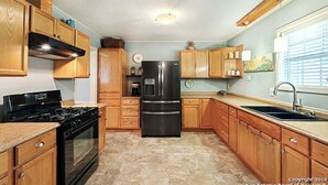 Una cocina con armarios de madera, un refrigerador negro, una estufa y un lavamanos.