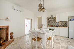 A modern kitchen with white cabinets, a dining table with a lace tablecloth, and a hanging light fixture.