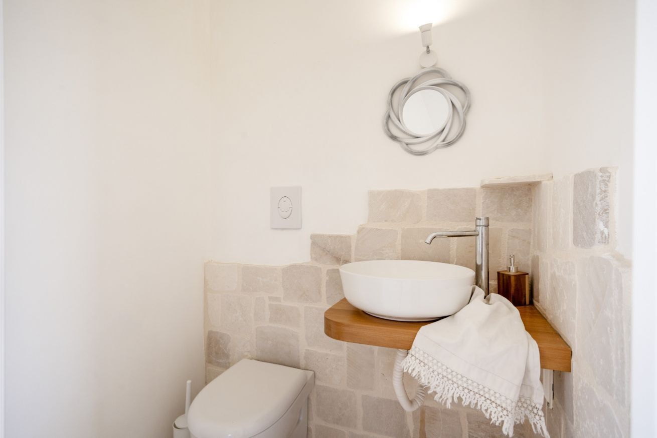 A bathroom with a stone wall, a white sink, a toilet, and a towel rack.