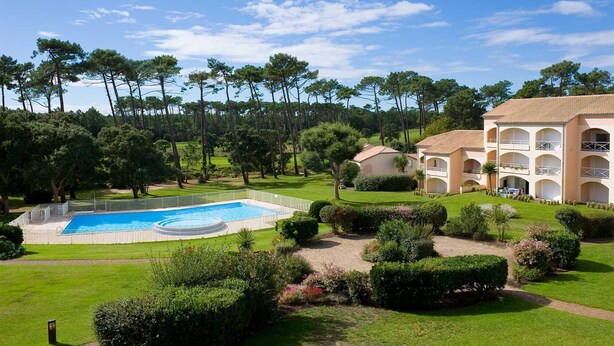 A pool surrounded by well-manicured lawns and trees, with a building featuring multiple balconies and a tiled roof. - Logement à 700m de la plage, sur le golf Moliets ! (Moliets)